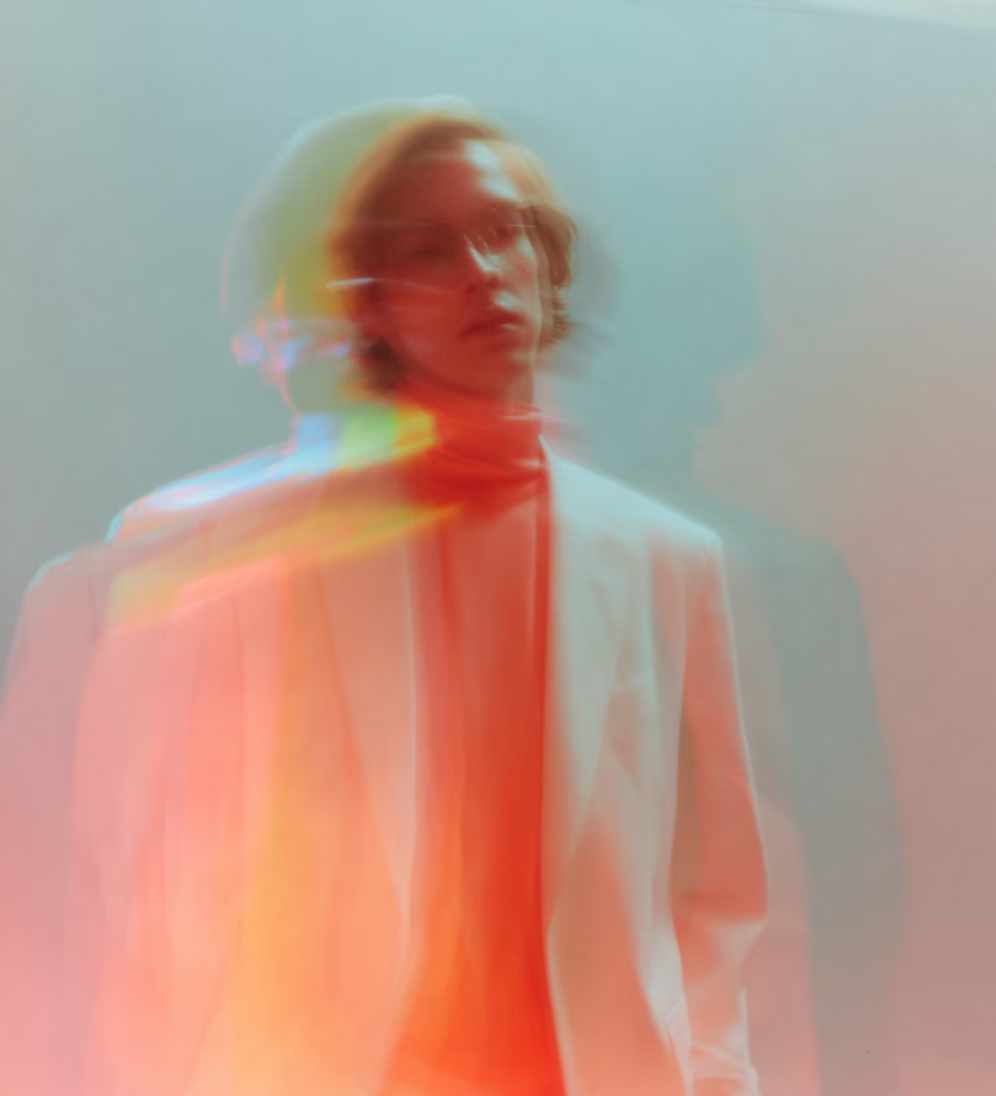 Blurred artistic portrait of a person wearing a white blazer and red shirt with color trails.