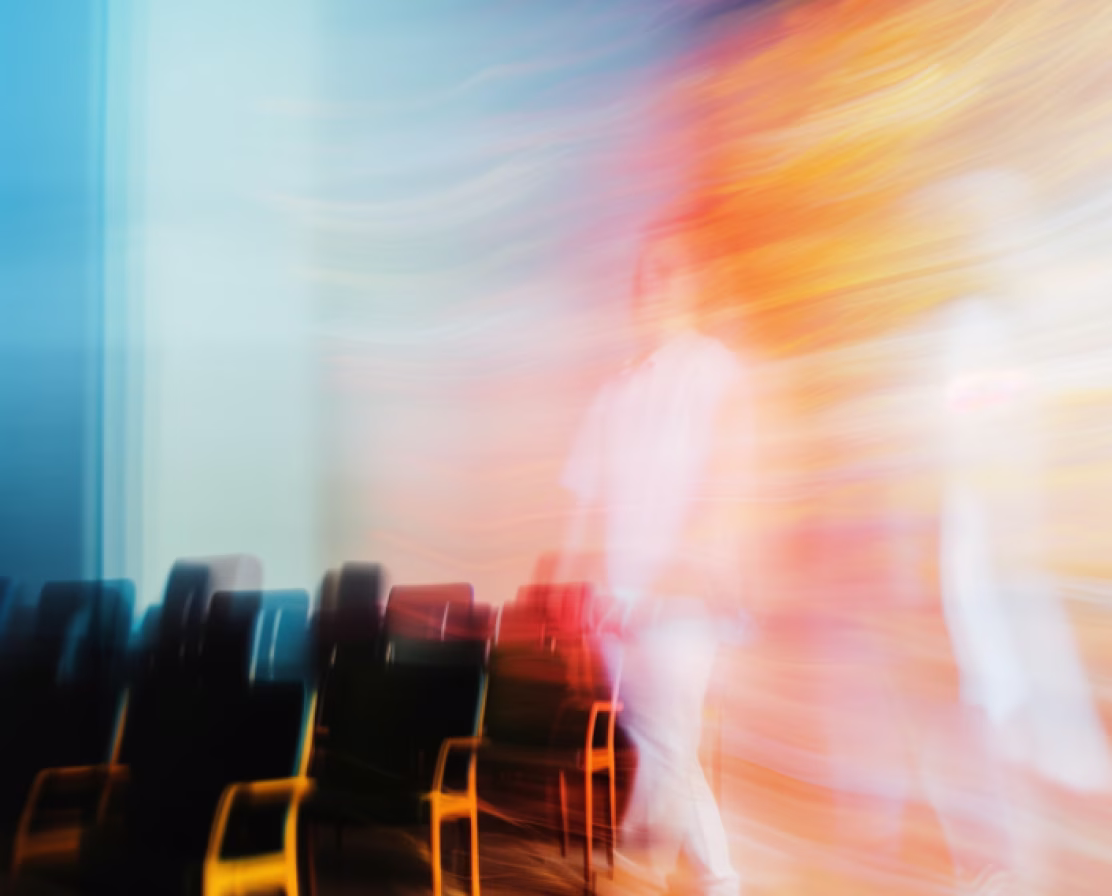 Blurred image of a person walking past rows of empty chairs with warm light streaks in the background.