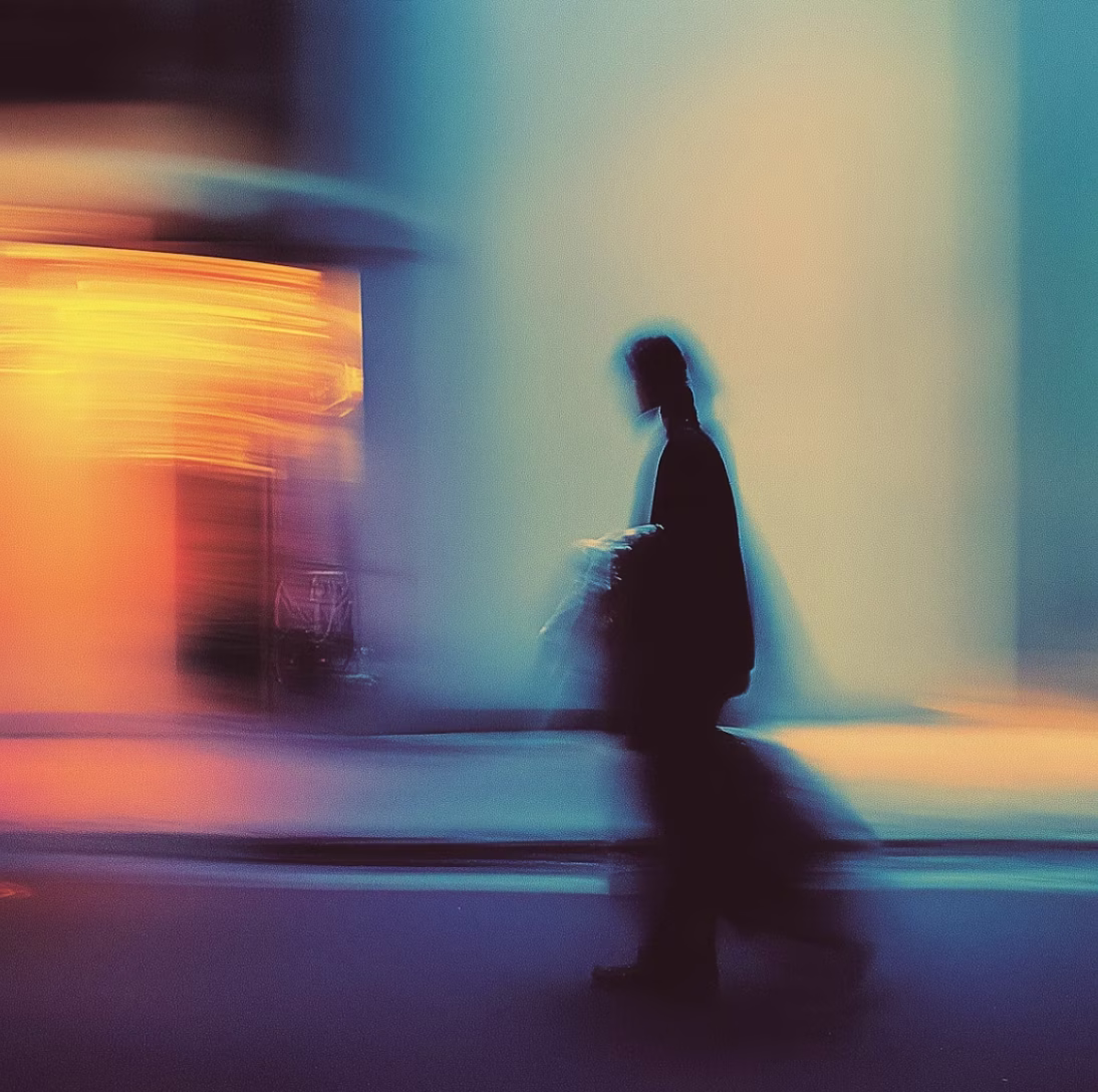 Blurred silhouette of a person walking past illuminated urban surroundings with blue and orange light streaks.