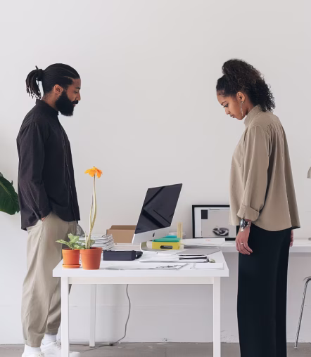 A man and woman standing on opposite sides of a white desk in a minimalist office setting.